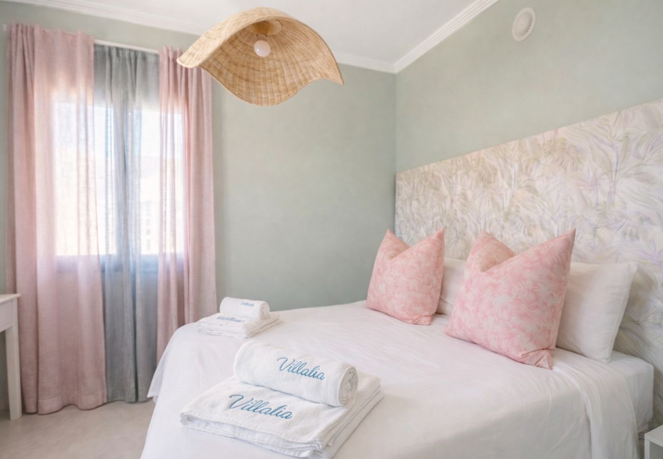 Cama doble con cojines rosas y pared verde